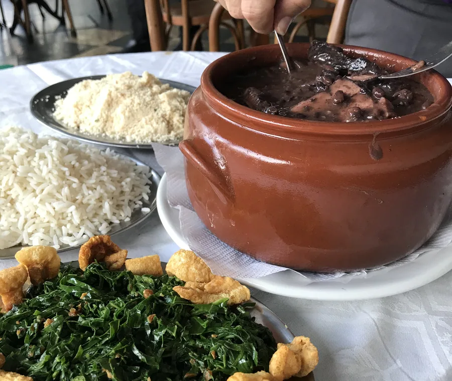 Hera's feijoada served in a clay pot with collard greens, rice and farofa