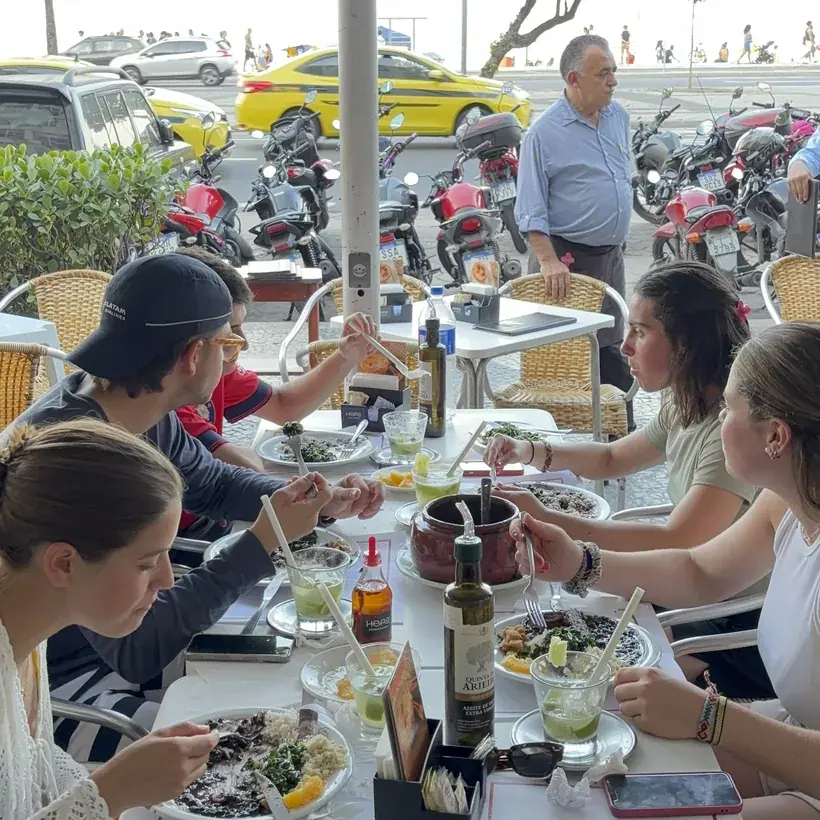 Sidewalk table at Hera with guests having lunch and Avenida Atlântica behind