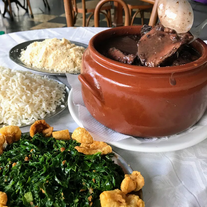 Hera's feijoada in a clay pot with collard greens, rice and farofa